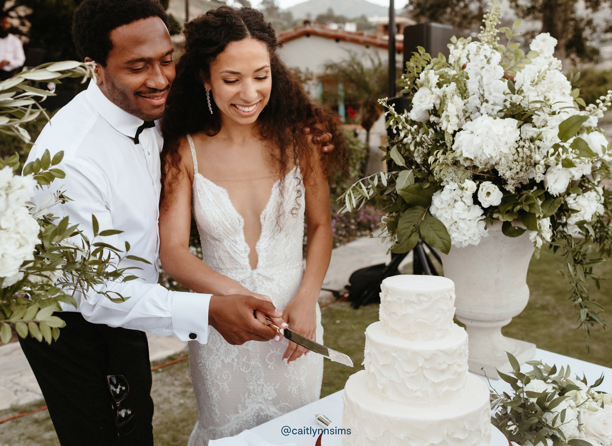 Newlyweds cutting a three tier white wedding cake