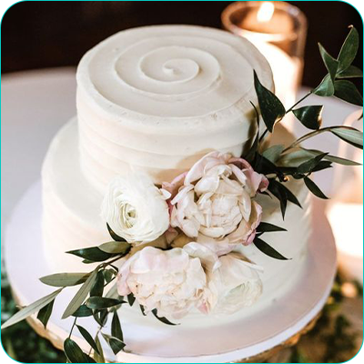 Two tier white wedding cake with peonies and swirl accent on top